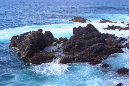 Ocean waves crashing onto the rocks in the sunset. Blue azure waterの写真素材