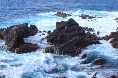 Ocean waves crashing onto the rocks in the sunset. Blue azure waterの写真素材