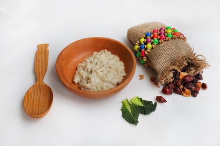 Oatmeal in a wooden bowl and dry berries in a bag. near a wooden spoon with sesame seeds on a white background. breakfastの写真素材