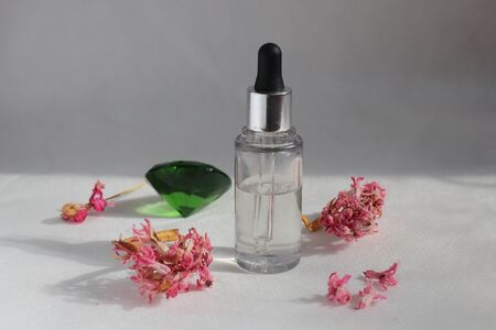 Dropper glass bottle with oil. Bottle with a cosmetic pipette. Antiaging moisturizing cosmetic product. Skin and body care. Pink oil essence flower product.の写真素材