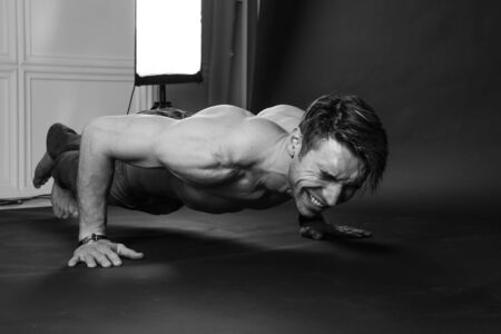 Muscular man doing push-ups on one hand against dark background. sexy bodyの写真素材