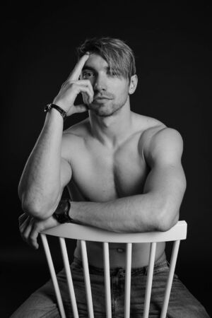 Muscular and fit young bodybuilder fitness male model posing on chair. Black and white photo. sexy body, smile and chorismの写真素材
