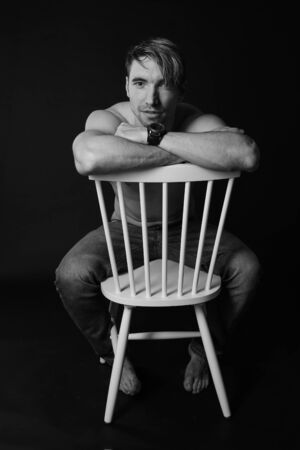 Muscular and fit young bodybuilder fitness male model posing on chair. Black and white photo. sexy body, smile and chorismの写真素材