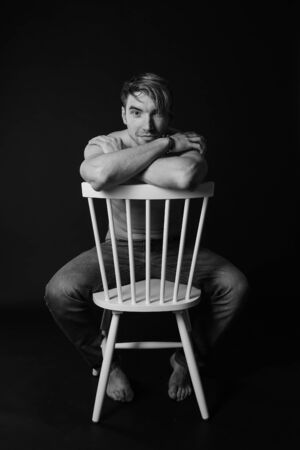 Muscular and fit young bodybuilder fitness male model posing on chair. Black and white photo. sexy body, smile and chorismの写真素材