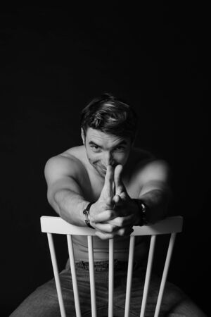 Muscular and fit young bodybuilder fitness male model posing on chair. Black and white photo. sexy body, smile and chorismの写真素材