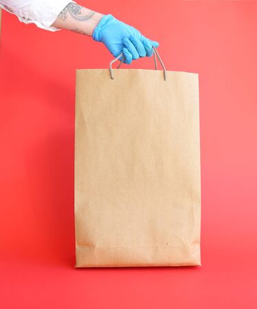 Hand holding a paper bag on a red, isolated. donation bagの写真素材