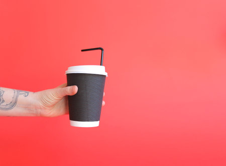 A paper cup of coffee in the hand. Black paper cup of coffee in hand. For mock up. Isolated. On red...