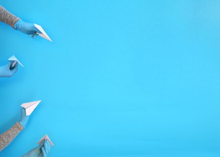 Hands in protective gloves of blue color are holding a paper airplane on a blue background. The concept of safe flights. Travel Quarantineの写真素材