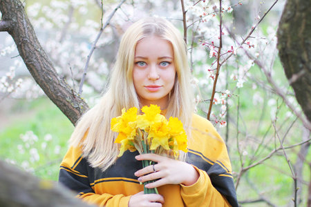 A beautiful young girl stands among the flowering trees. A girl with white hair, in a Yellow...