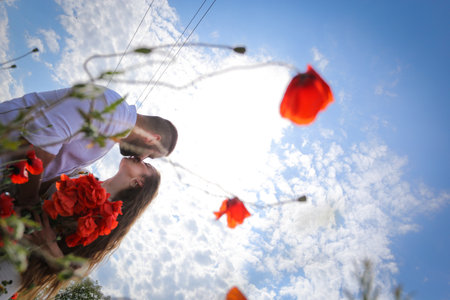 Loving couple in the poppy field. The guy gently kisses his girlfriend in the neck. Loving couple hug one another during romantic date in poppy field. Enjoying time together. Passion.の写真素材