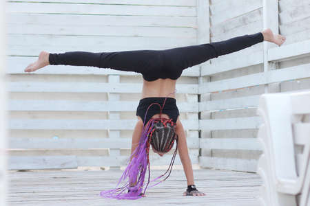 a gymnast in a black swimsuit performs splits on her hands on a white isolated background with space for textの写真素材