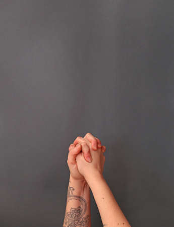 intertwined fingers of female hands with a tattoo on a gray background. help and mutual assistance conceptの写真素材