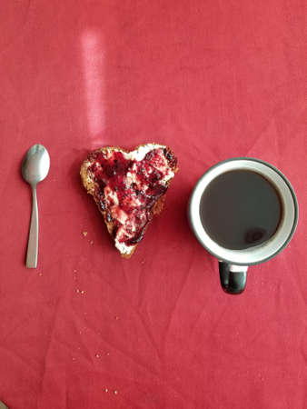Top view, a cup of coffee, a spoon, a sandwich with jam on a red tablecloth. concept i love youの写真素材