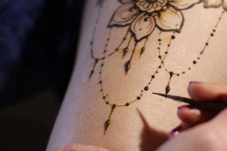 Image detail of henna being applied to hand. a lot of jewelry on the arms, bare belly. partial focus, art blur.の写真素材