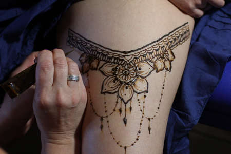 Image detail of henna being applied to hand. a lot of jewelry on the arms, bare belly. partial focus, art blur.の写真素材