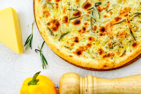 hot pizza with onions and basil on a wooden surface with vegetables on a white tableの写真素材
