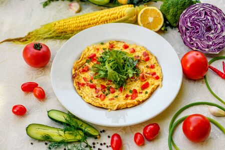 egg omelet with cherry tomatoes, cheese and arugula on a plate on the table with a white tableclothの写真素材