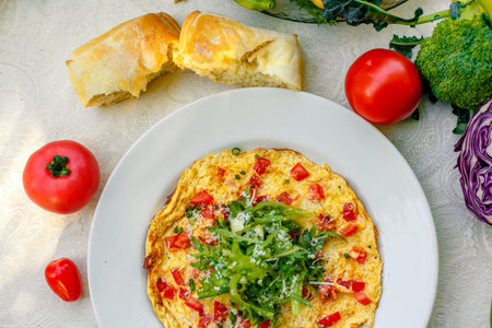 egg omelet with cherry tomatoes, cheese and arugula on a plate on the table with a white tableclothの写真素材