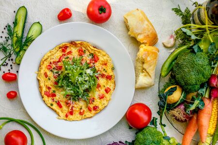 egg omelet with cherry tomatoes, cheese and arugula on a plate on the table with a white tableclothの写真素材