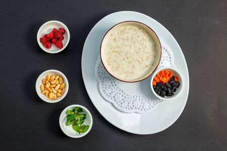 rice porridge with milk, healthy breakfast with raisins, nuts, mint on a white plateの写真素材
