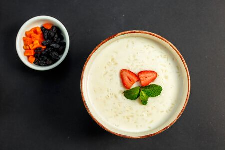 rice porridge with milk, healthy breakfast with raisins, nuts, mint on a white plateの写真素材
