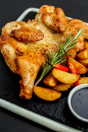 appetizing grilled chicken with homemade potatoes and sauce on a black trayの写真素材