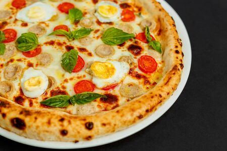 delicious Italian pizza with chicken sausages, eggs and basil on a black tableの写真素材