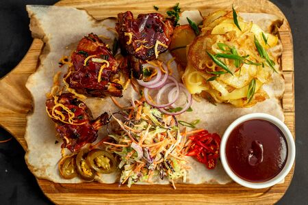 hot appetizing ribs with homemade potatoes, salad and sauce on a wooden boardの写真素材