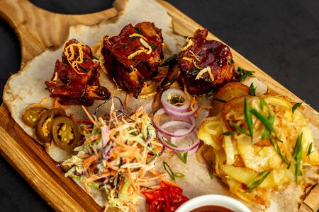 hot appetizing ribs with homemade potatoes, salad and sauce on a wooden boardの写真素材