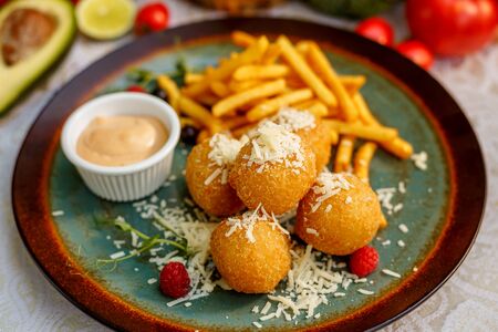 Crispy potato balls with soft melted cheese and french fries on decorated tableの写真素材