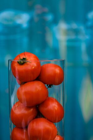 red tomatoes in a glass flask on a blue background with space for textの写真素材