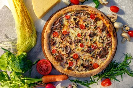 Delicious italian pizza served on table with ingredients cheese and vegetablesの写真素材