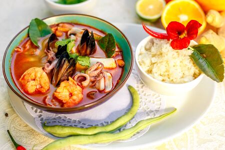 Thai soup tom yam with seafood (octopus, shrimps), herbs and vegetables served on the table with ingredients, healthy foodの写真素材