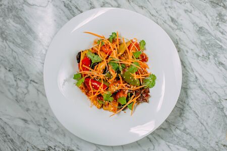 Vegetarian tomato, olives pepper salad in a white plate on a marble table, healthy foodの写真素材
