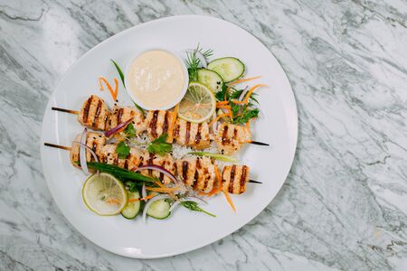 chicken kebabs with rice in a white plate on a marble tableの写真素材
