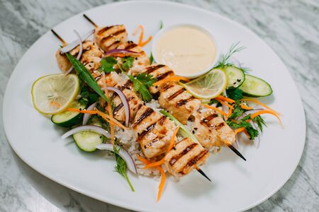chicken kebabs with rice in a white plate on a marble tableの写真素材
