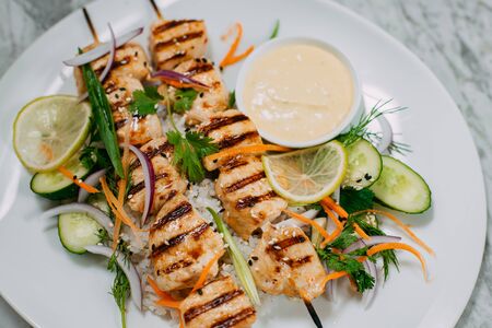 chicken kebabs with rice in a white plate on a marble tableの写真素材