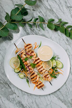 chicken kebabs with rice in a white plate on a marble tableの写真素材
