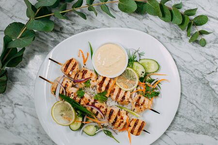 chicken kebabs with rice in a white plate on a marble tableの写真素材