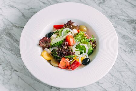 Vegetarian tomato, olives pepper salad in a white plate on a marble table, healthy foodの写真素材