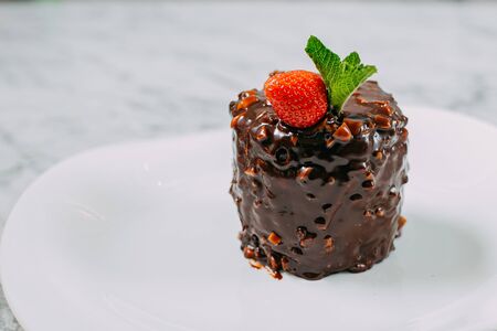 chocolate cake with nuts, strawberries and mint in a white plate on a marble tableの写真素材