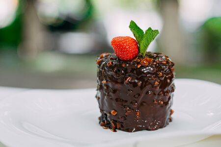 chocolate cake with nuts, strawberries and mint in a white plate on a marble tableの写真素材