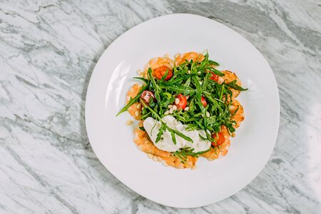 salad with shrimp, cheese and arugula in a white plate on a marble tableの写真素材