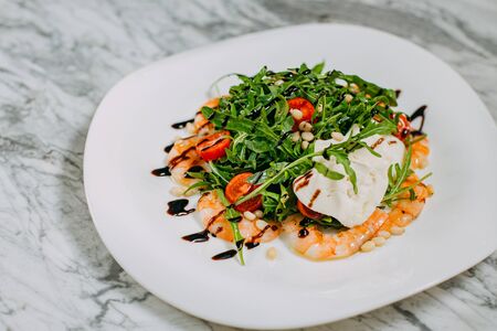 salad with shrimp, cheese and arugula in a white plate on a marble tableの写真素材
