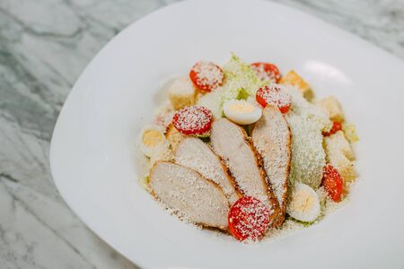 Caesar salad with chicken crackers and cheese in a white plate on a marble tableの写真素材