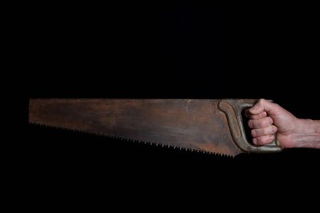 closeup of a hand of an elderly man holding old vintage rusty saw isolated on black backgroundの写真素材