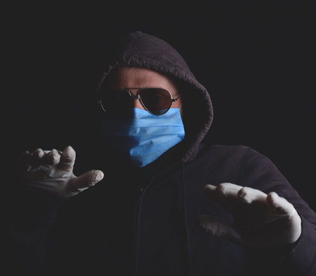 closeup of scared man in blue surgical antiviral mask, sterile gloves, sunglasses and a hood...