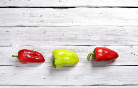 two red and one yellow peppers on old rustic white wooden tableの写真素材