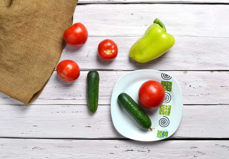still life with tomatoes, cucumbers, pepper and white plate with ornament on an old wooden light rustic table with an old bagの写真素材
