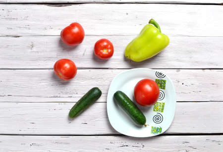still life with tomatoes, cucumbers, pepper and plate with ornament isolated on an old wooden light rustic tableの写真素材